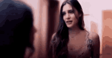 a woman with long hair is standing next to another woman in a room and talking to her .