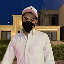 a man wearing a white shirt and a black mask is standing in front of a building