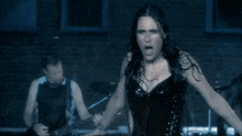 a woman in a black corset is singing in front of a man playing a guitar