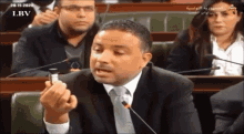 a man in a suit and tie is speaking into a microphone in front of a l.b.v. logo