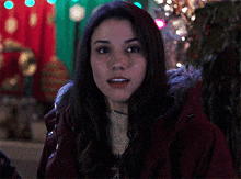 a woman wearing a red jacket with a fur hood looks at the camera