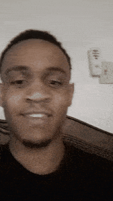 a man in a black shirt is smiling with a remote control hanging on the wall behind him