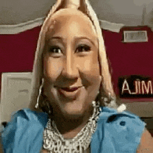 a woman wearing a blue shirt and a necklace is smiling for the camera .