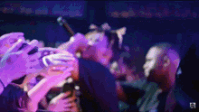 a blurry photo of a man holding a microphone in front of a crowd with purple lights