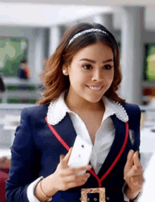 a woman in a school uniform is holding a cell phone in her hand and smiling .