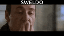 a man is covering his mouth with his hands in a close up of a movie scene .
