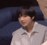 a young man in a white shirt is sitting on a couch and making a funny face .