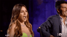 a woman in a neon green dress is standing next to a man in a suit with the nbc logo on the bottom right
