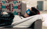 a woman laying on a couch wearing a blue eye mask