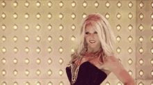 a woman in a black dress is dancing in front of a wall with lights on it .