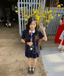 a girl giving a peace sign in front of a tree