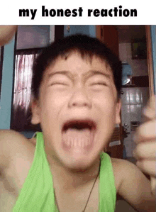 a young boy in a green tank top is crying with his mouth wide open .