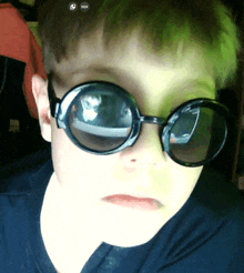 a close up of a child wearing sunglasses with a red sticker on the bottom right corner