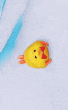 a yellow rubber duck with a red bow on its head is sitting on top of a white surface .