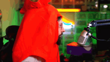 a man in a red hoodie stands in front of a microphone with a green background