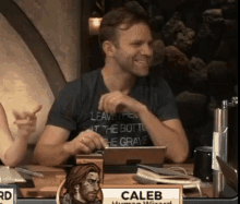 a man is sitting at a table with a tablet and a sign that says caleb human wizard .