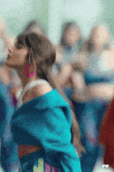 a woman wearing a blue jacket and pink earrings is dancing in a crowd .