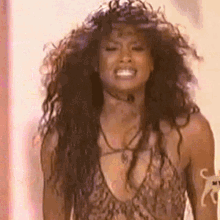 a woman with long curly hair is wearing a leopard print tank top and necklace .