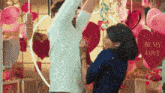 a man and a woman are dancing in front of a wall with hearts and balloons and a sign that says be my love