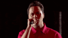 a man in a red shirt is singing into a microphone on stage .