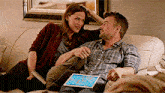 a man and a woman are sitting on a couch with a tablet in front of them