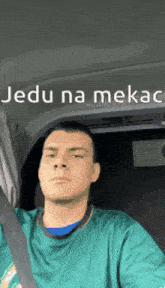 a man in a green shirt is sitting in a car with the words jedu na mekac on the bottom