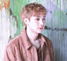 a young man wearing a brown jacket and tie stands in front of a graffiti covered wall