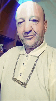 a bald man wearing a white shirt and a necklace that says ' sdf ' on it