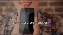a woman is holding a cell phone with the words life is like a box of chocolates