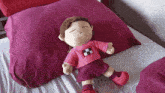 a stuffed doll laying on a bed with a pink pillow