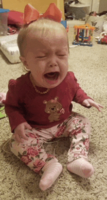 a baby with a bow on her head is crying on the floor