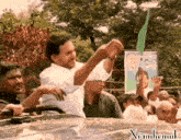 a man in a white shirt holds up a green object in front of a sign that says ' xianhemuk ' on it