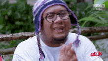 a man wearing a knitted hat and glasses is sitting in front of a fence ..
