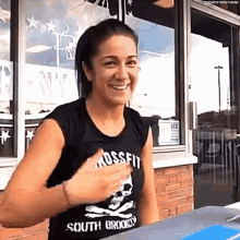 a woman wearing a crossfit shirt is smiling while sitting at a table .