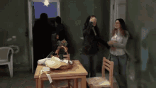 two women standing in a room with a table and chairs and a basket on it
