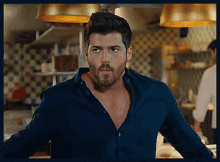 a man with a beard is standing in a kitchen wearing a blue shirt