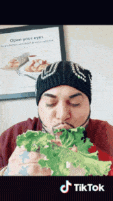 a man eating lettuce in front of a sign that says open your eyes