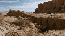 a man stands on top of a cliff next to a car that has fallen off the side of the road