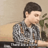 a young boy in a plaid shirt is sitting on a couch and saying there are a knife