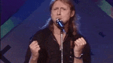 a man is singing into a microphone while holding his fists in the air .