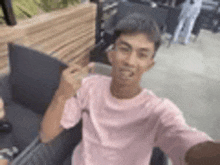 a man in a pink shirt is taking a selfie while sitting on a chair .