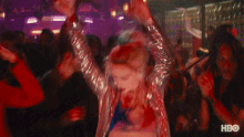 a woman in a silver dress is dancing in a crowd with hbo written on the bottom left