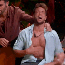 a shirtless man is laughing while a man holds his arm around his shoulder .