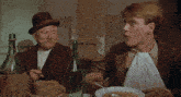 two men are sitting at a table with bowls of soup and a bottle of wine
