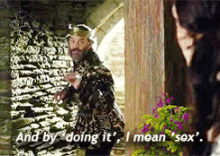 a man with a beard is standing in front of a stone wall and says and by doing it i mean sex