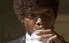 a man with curly hair and a beard is drinking from a cup .