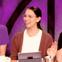 a woman wearing glasses is sitting at a table with a tablet in front of her