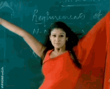 a woman in a red shirt is standing in front of a blackboard with her arms in the air .