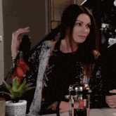 a woman sitting at a table with a french press in her hand