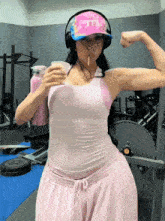 a woman in a pink tank top and pink sweatpants is flexing her arm
